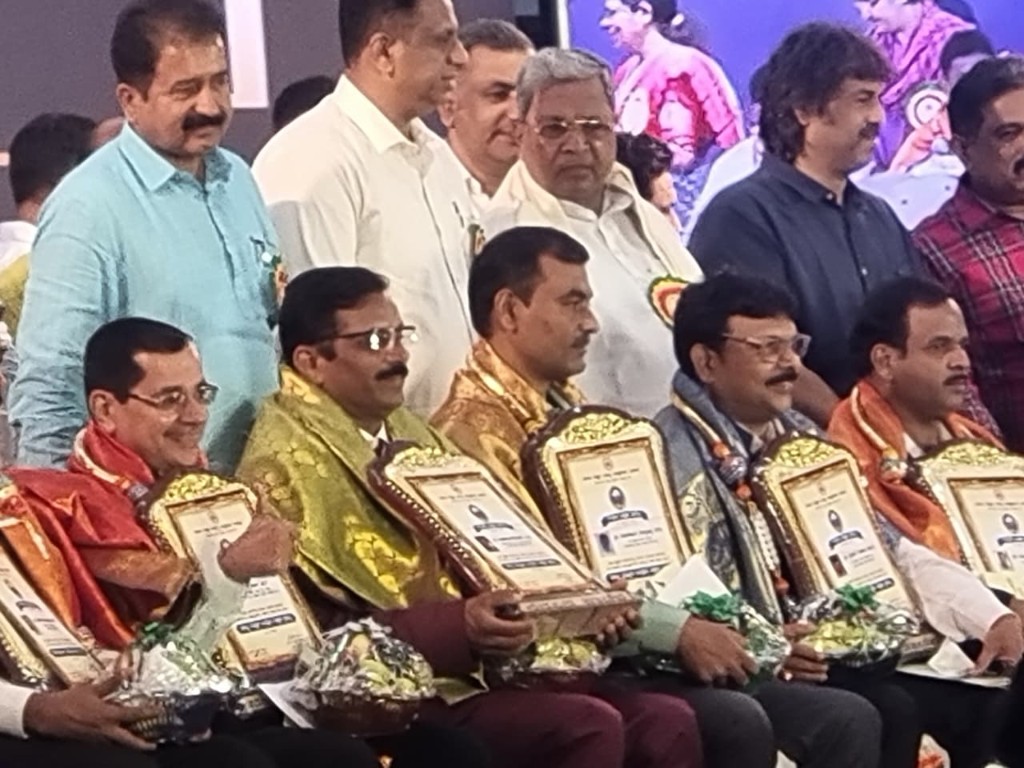 Group photo at an award ceremony with seated awardees holding plaques and dignitaries standing behind