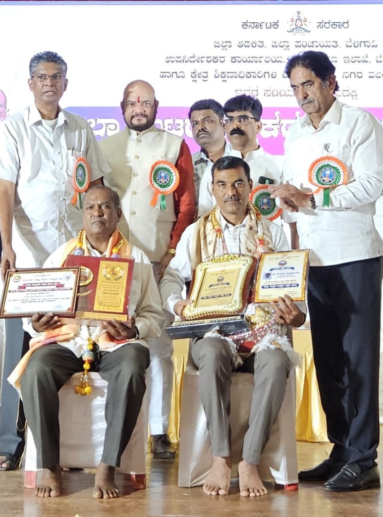 Award ceremony on stage with officials and large Kannada banner, seated awardees with plaques