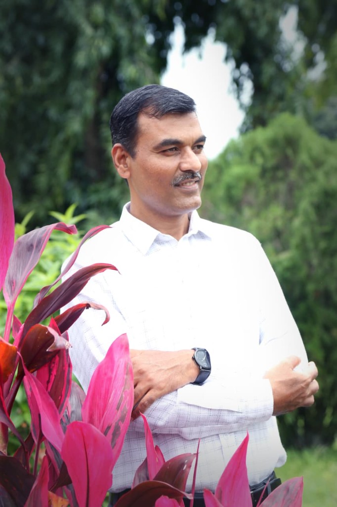 Rajashekhar Ragati outdoors, arms crossed, smiling, with green foliage behind him